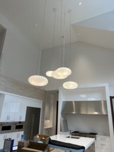 A modern kitchen with a set of five dome-shaped pendant lights above a central island. The kitchen features stainless steel appliances and white cabinetry.