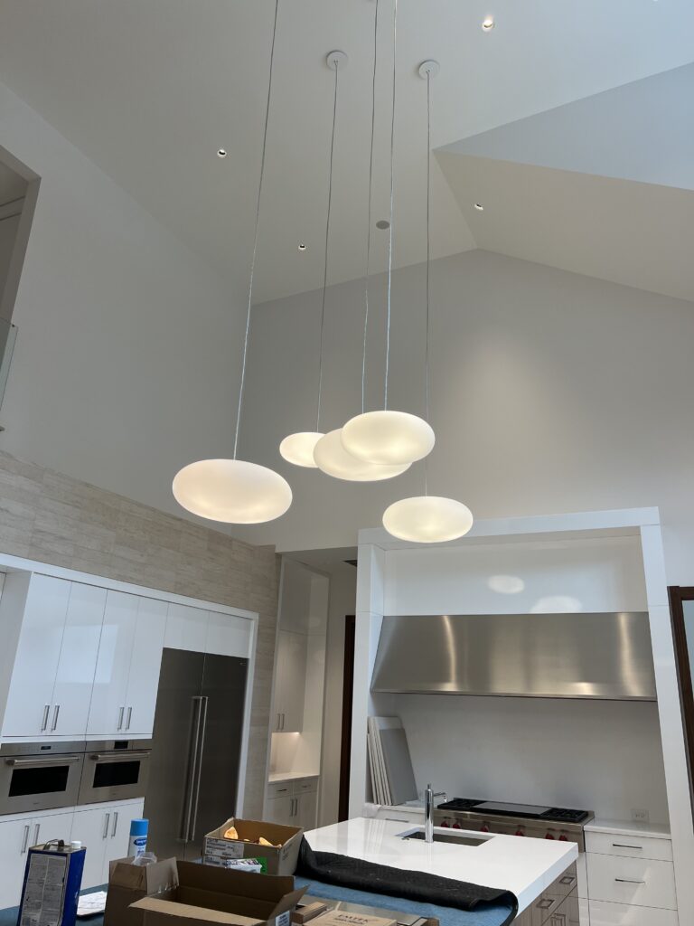 A modern kitchen with a set of five dome-shaped pendant lights above a central island. The kitchen features stainless steel appliances and white cabinetry.