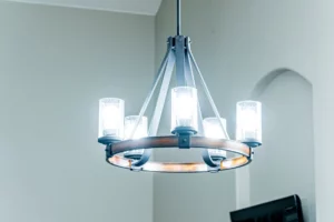 A modern chandelier with five lit glass-covered bulbs hangs from the ceiling in a neutral-colored room.