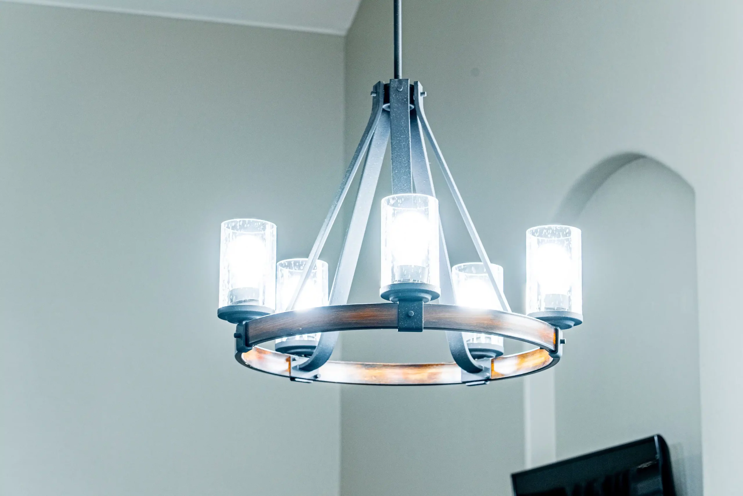 A modern chandelier with five lit glass-covered bulbs hangs from the ceiling in a neutral-colored room.