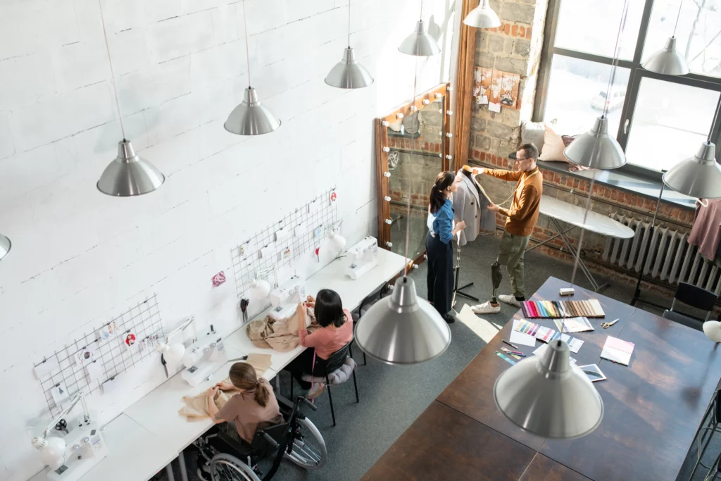 How Commercial Lighting Installation Cuts Energy Costs by 40%: Real Data from 100 Businesses 2 A scene showing good commercial lighting installation – People work at sewing stations in a bright studio; two stand by a clothing rack while others sit at desks.